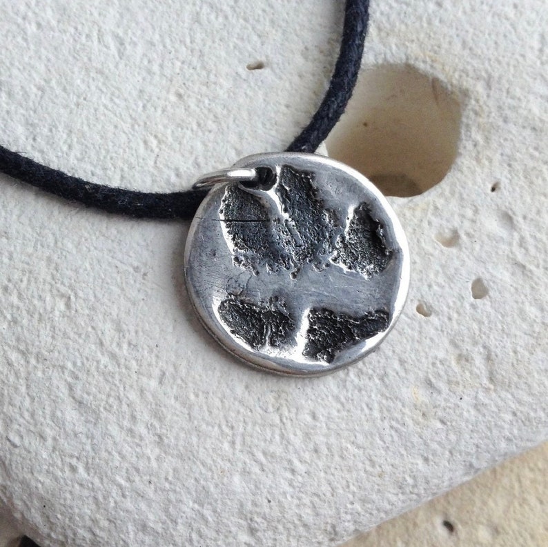 May include: A silver necklace with a round pendant featuring a detailed paw print design. The necklace is on a black cord.