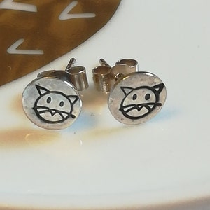 May include: A pair of silver stud earrings with a black cat face design.