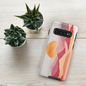 May include: A phone case featuring an abstract design of mountains and a sun in a range of colours. The case is black and has a cut-out for the camera lens.