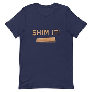 May include: A navy blue t-shirt with the text "SHIM IT!" in orange lettering and a small image of a wooden shim.
