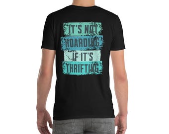 Puede incluir: Camiseta negra con el texto "IT'S NOT HOARDING IF IT'S THRIFTING" en un diseño desgastado y en capas. El texto utiliza tonos de azul y turquesa. La camiseta tiene cuello redondo y una estética vintage.