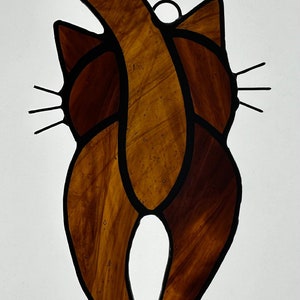 May include: A stained glass cat figurine with a brown and black color scheme. The cat is facing away from the viewer with its tail curled up over its back.