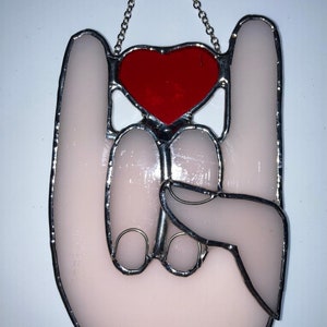 May include: A stained glass ornament shaped like a hand making the 'I love you' sign with a red heart in the center.