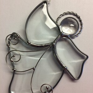 May include: A clear glass angel ornament with silver wire detailing and a crystal halo. The angel has a simple design with a rounded body and wings.