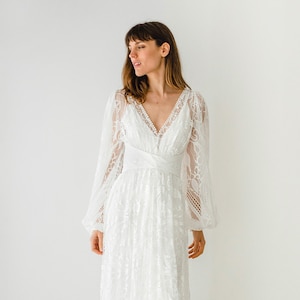 May include: A white lace wedding dress with long sleeves and a V-neckline. The dress has a fitted bodice and a flowing skirt.