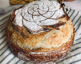 May include: A freshly baked loaf of sourdough bread with a spiral design on top. The bread has a golden brown crust and is sitting on a white and blue striped kitchen towel.