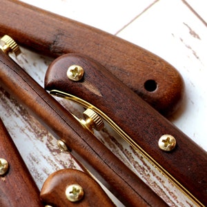 May include: Close-up of several wooden knife handles with brass accents and screws. The handles are a rich, dark brown color, and the brass details provide a contrast. The arrangement suggests a set of knives or similar tools.