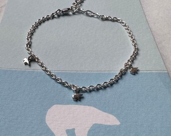 Può includere: Un braccialetto a catena d'argento con tre piccoli ciondoli a forma di orso d'argento. Il braccialetto è su uno sfondo blu e bianco.