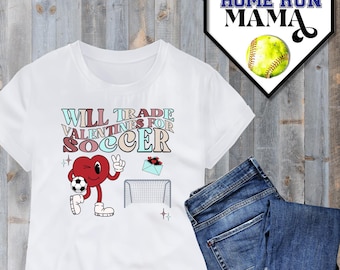 May include: White t-shirt with a pink, blue, and red graphic that says "Will Trade Valentines for Soccer". The graphic features a cartoon heart holding a soccer ball and standing next to a soccer goal.