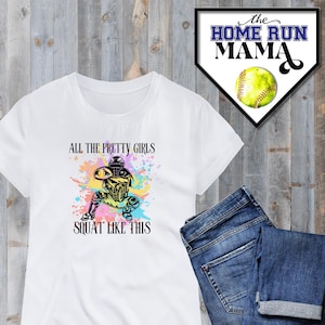 Peut inclure: T-shirt blanc avec un graphique coloré d'une joueuse de softball en position de receveur. Le texte "All the pretty girls squat like this" est imprimé sur le t-shirt.