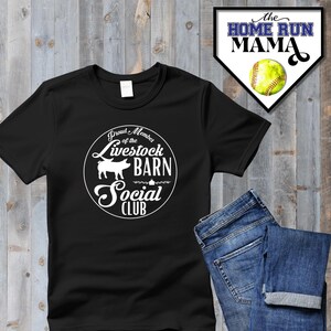 Può includere: Maglietta nera con un grafico circolare bianco che dice "Proud Member of the Livestock Barn Social Club". Il grafico presenta anche una silhouette di maiale bianca.