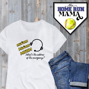 Puede incluir: Camiseta blanca con auriculares negros y el texto "ma'am Ma'am MA'AM What's the address of the emergency?" en amarillo. La camiseta está sobre un fondo de madera con una tela vaquera azul en la esquina inferior derecha.