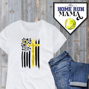 Puede incluir: Camiseta blanca con un gráfico negro y amarillo de una cruz y una bandera estadounidense. El texto "Always Heard, Never Seen" está en la cruz. La camiseta está sobre una superficie de madera con un par de pantalones vaqueros azules.
