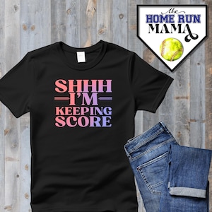 May include: Black t-shirt with the text "SHHHH - I'M - KEEPING SCORE" in pink and purple gradient lettering. The text is in a retro font style.