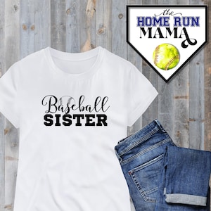 Op de afbeelding: Wit T-shirt met zwarte tekst die "Baseball Sister" zegt en een kleine zwart-witte baseball afbeelding. Het Home Run Mama logo is op de achtergrond.