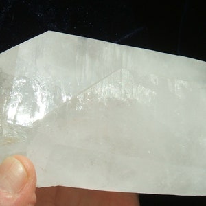 May include: A large, clear quartz crystal with multiple facets and a pointed tip. The crystal is translucent and has a slight milky hue.