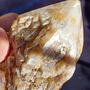 May include: A clear quartz crystal with a brown, layered, and textured base. The crystal has a pointed tip and is a natural, raw specimen.