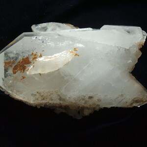 May include: A large, clear quartz crystal cluster with a rough, natural texture. The crystal has a milky white color and is accented with brown inclusions.