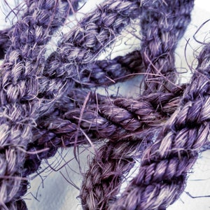 May include: Close-up of a thick, purple rope with a frayed texture. The rope is woven together in a tight braid.