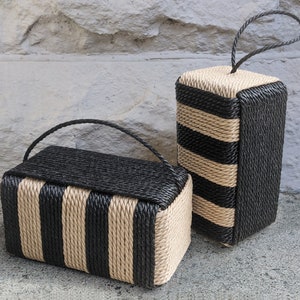 May include: Two black and tan striped rope doorstops. The larger doorstop has a loop handle. The smaller doorstop has a rectangular shape.