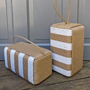 May include: Two doorstops made of woven rope with white stripes. The doorstops are rectangular and have a handle on the top.