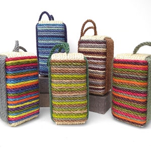 May include: A collection of rectangular doorstops, each crafted from colorful, tightly wound rope. The doorstops feature a variety of colors, including blue, green, brown, and rainbow stripes. Each doorstop has a rope handle. The doorstops are a decorative home accent.