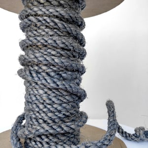 May include: A spool of thick, gray rope with a rough texture. The rope is wound tightly around the spool and is ready to be used for crafting or other projects.
