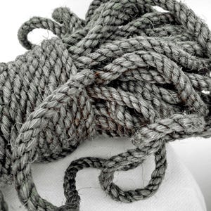 May include: Close-up of a coiled gray rope. The rope is thick and appears to be made of natural fibers. The texture of the rope is visible, with individual strands twisted together. The rope is likely used for nautical or decorative purposes.