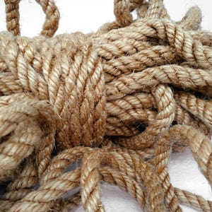 May include: A close-up of a thick, natural fiber rope, tightly coiled and knotted. The rope is a light brown color and has a rough, textured surface.