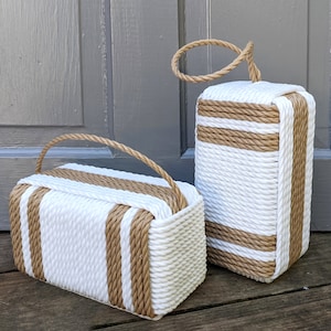 May include: Two doorstops made of woven rope, one with a handle and one with a loop. The doorstops are white with brown rope accents.