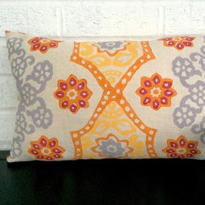 May include: Rectangular decorative pillow with a cream-colored background and a repeating pattern of orange, yellow, and purple floral and geometric shapes. The pillow is a home decor item.