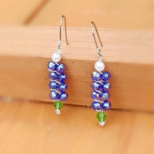 May include: A pair of dangle earrings with a silver hook, a white pearl bead, and a cascade of blue and green crystal beads.