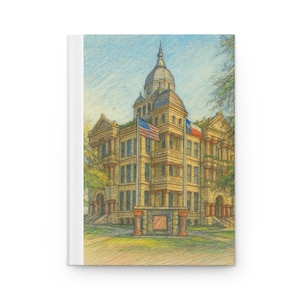 May include: A hardcover journal featuring a colored pencil illustration of a historic building with a dome, flags, and columns. The building is beige with a blue sky background. The journal has a white spine.