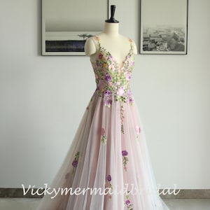 May include: A light pink wedding dress with a V-neckline and floral embroidery. The dress features a flowing tulle skirt and is displayed on a mannequin. The text "Vickymermadbridal" is visible on the dress.