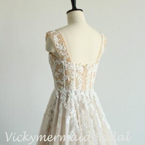 May include: A sleeveless, ivory wedding dress with a fitted bodice and a flowing skirt. The bodice is covered in delicate lace and the skirt is made of tulle. The dress is shown on a mannequin.