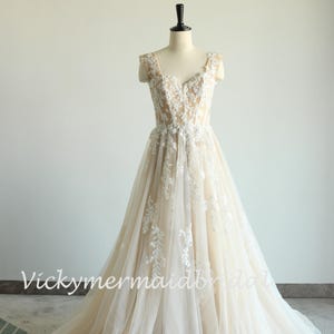 May include: A sleeveless, ivory wedding dress with a sweetheart neckline and delicate floral lace appliques. The dress has a fitted bodice and a flowing A-line skirt.