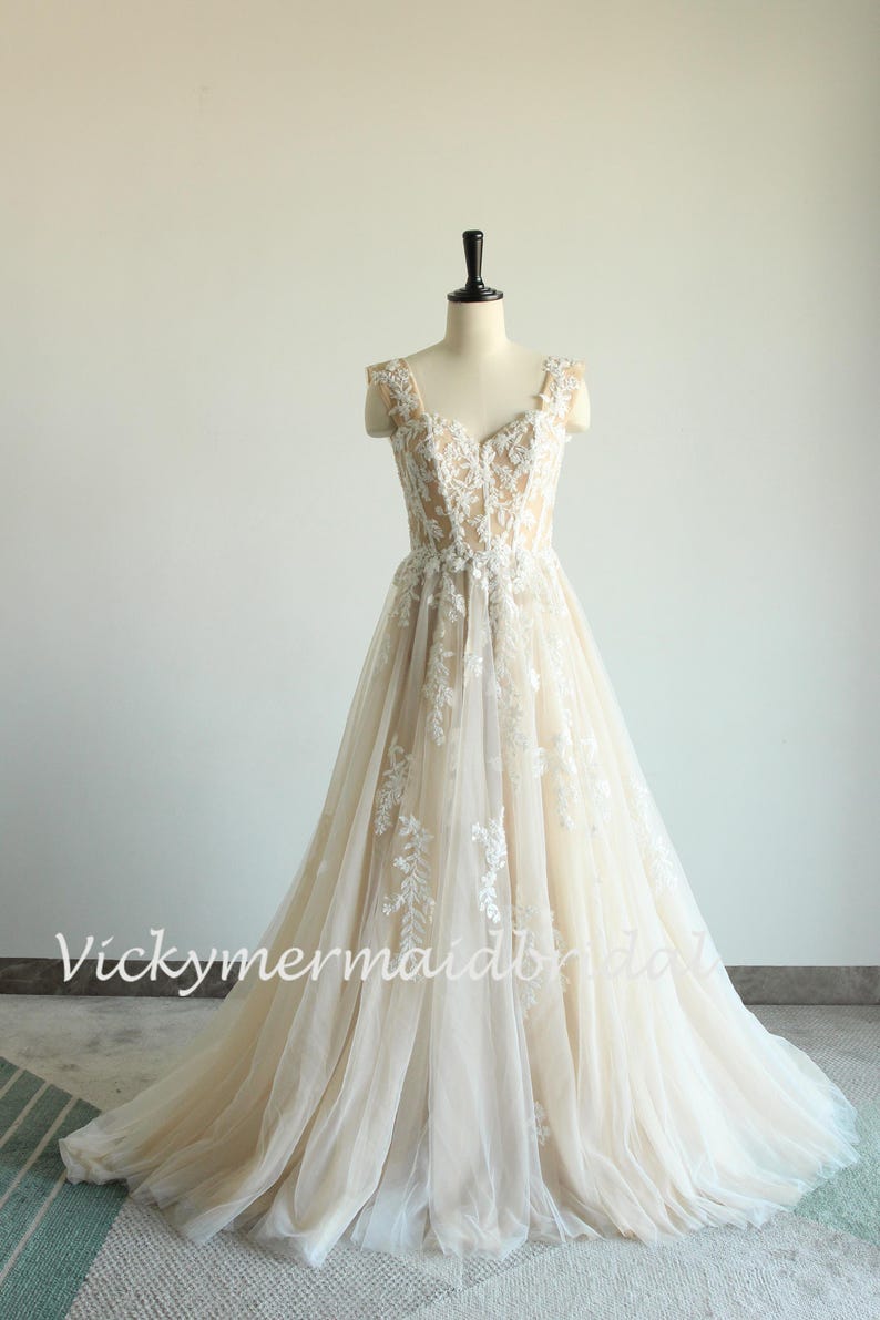 May include: A sleeveless, ivory wedding dress with a sweetheart neckline and delicate floral lace appliques. The dress has a fitted bodice and a flowing A-line skirt.
