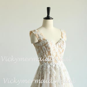 May include: A sleeveless, ivory wedding dress with a sweetheart neckline and delicate lace detailing. The dress has a fitted bodice and a flowing skirt.