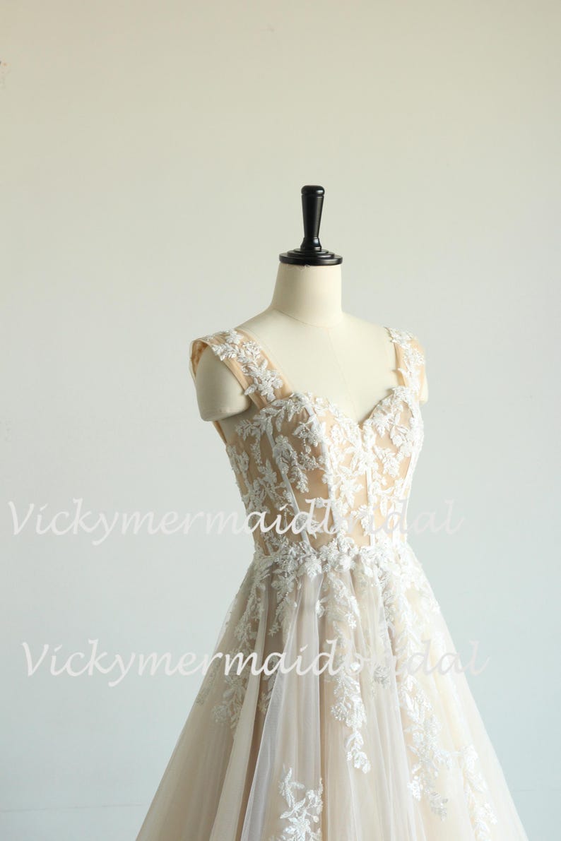 May include: A sleeveless, ivory wedding dress with a sweetheart neckline and delicate lace detailing. The dress has a fitted bodice and a flowing skirt.