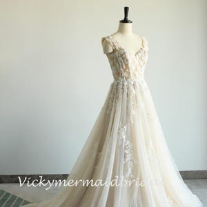 May include: A sleeveless, ivory wedding dress with a sweetheart neckline and delicate floral lace embroidery. The dress has a flowing A-line skirt and a sheer tulle overlay.