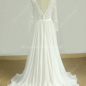 May include: A white chiffon wedding dress with long lace sleeves and a deep V-neckline. The dress has a fitted bodice and a flowing skirt.