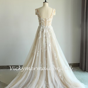 May include: A long, flowing wedding dress with a lace bodice and a tulle skirt. The dress has a sweetheart neckline and cap sleeves. The dress is ivory in color and has a train.