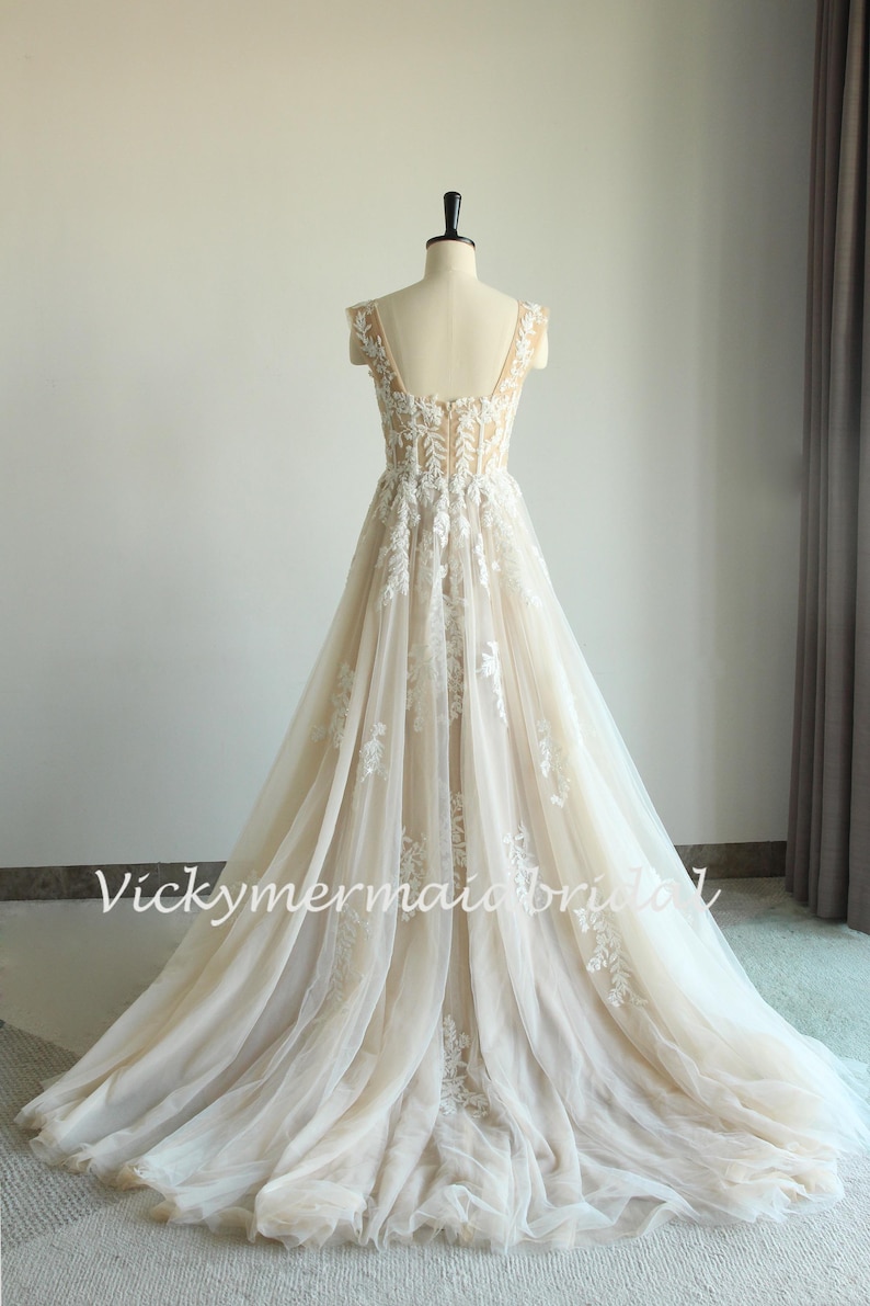 May include: A long, flowing wedding dress with a lace bodice and a tulle skirt. The dress has a sweetheart neckline and cap sleeves. The dress is ivory in color and has a train.