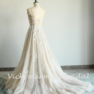 May include: A white and beige wedding dress with a lace bodice and a tulle skirt. The dress has a V-neckline and a fitted bodice. The skirt is full and flowing. The dress is on a mannequin.