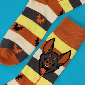 May include: A pair of colourful socks with a striped pattern and a bat design. One sock features a cartoon bat with fangs and a dripping tongue.