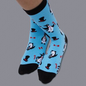 May include: A pair of blue socks with a pattern of penguins wearing top hats and bow ties. The socks have black toes and heels.