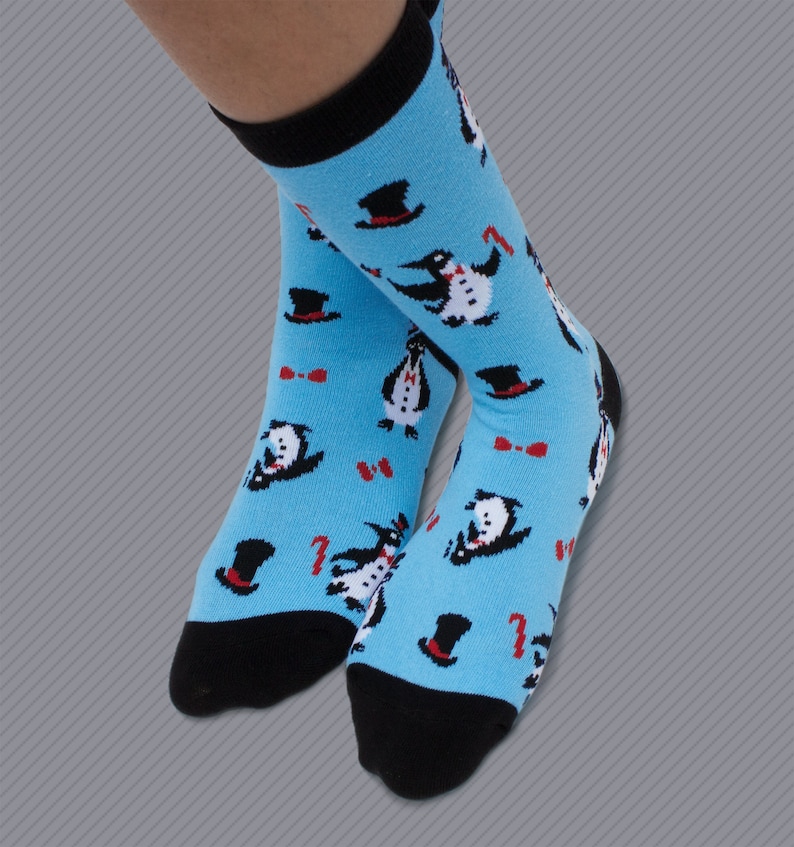 May include: A pair of blue socks with a pattern of penguins wearing top hats and bow ties. The socks have black toes and heels.