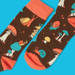 May include: A pair of brown socks with a colorful pattern of mushrooms, snails, and houses. The socks have orange cuffs.