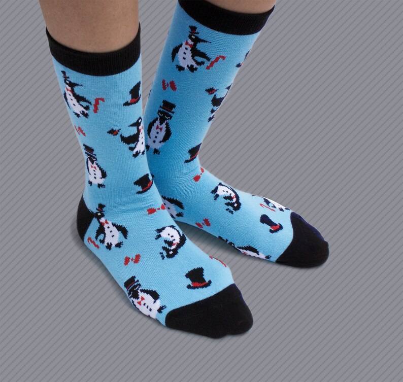 May include: A pair of blue socks with a black cuff and a pattern of penguins wearing top hats and bow ties.