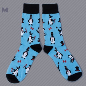 May include: A pair of blue socks with a pattern of penguins wearing top hats and bow ties. The socks have black cuffs.